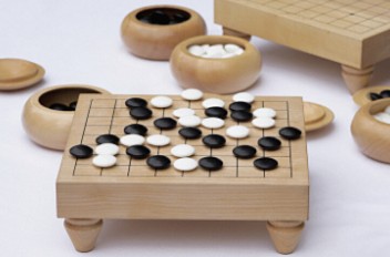 木製の碁盤に並んだ黒石と白石、碁笥